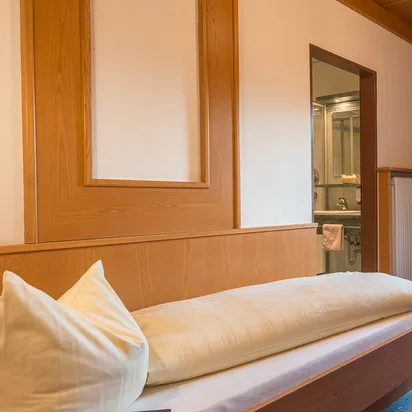 Cozy single hotel room with wooden furniture, balcony view, and ensuite bathroom